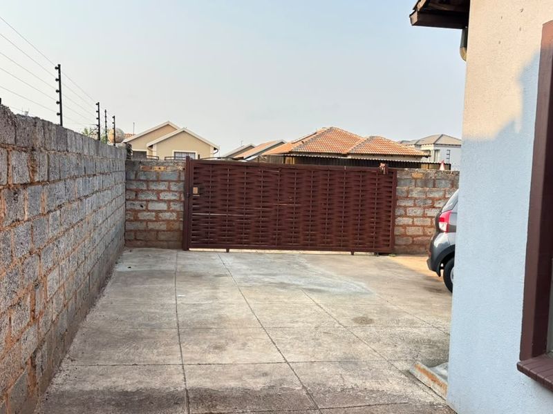 A paved driveway area featuring a sliding gate, perimeter wall with electric fencing, and security bars on the window.