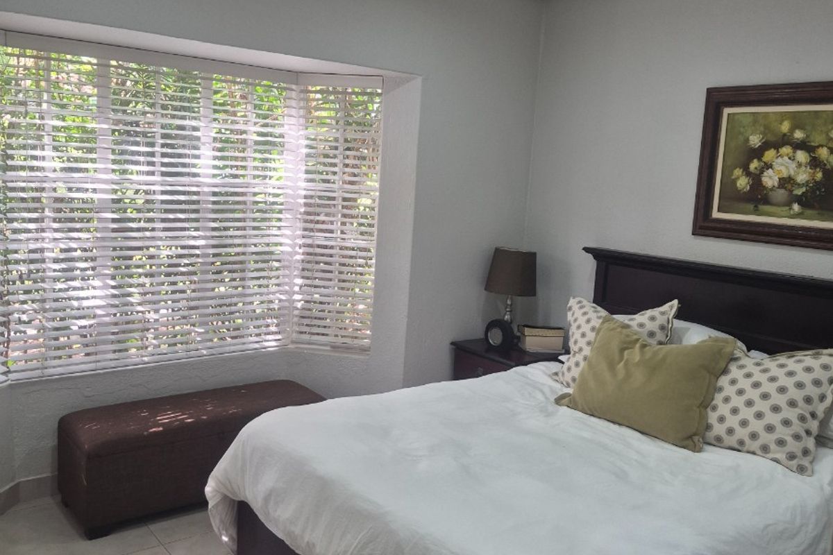 A well-maintained bedroom featuring tiled flooring, a ceiling fan, and a large bay window that allows for natural light.