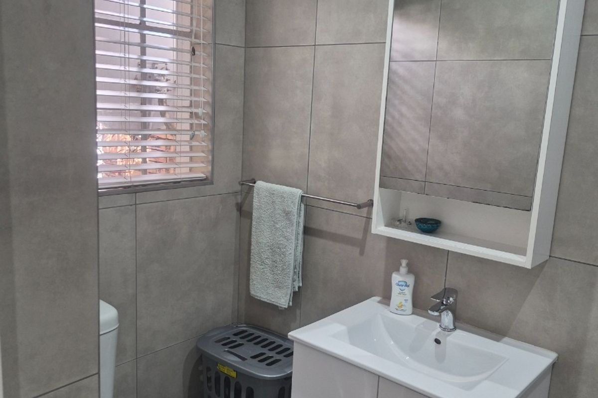 Modern bathroom featuring floor-to-ceiling grey tiling, a white vanity cabinet with integrated basin, wall-mounted storage cabinet, and a toilet.