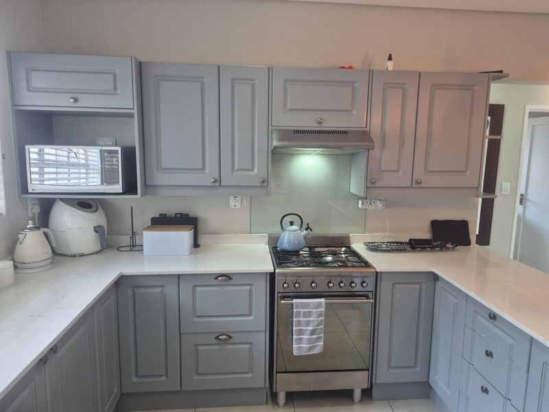 Modern kitchen featuring grey shaker-style cabinetry, quartz countertops, a glass splashback, and a stainless steel gas stove with an integrated extractor fan.