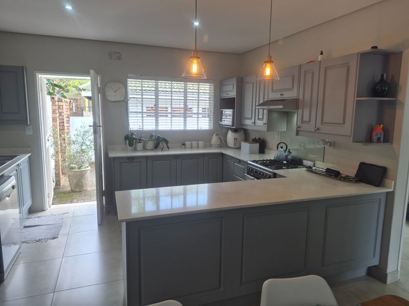 Modern kitchen featuring grey cabinetry, stone countertops, gas hob, and direct access to an outdoor area, creating a functional and bright cooking space.