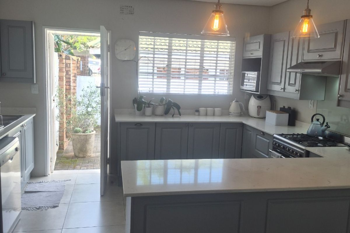 Modern U-shaped kitchen featuring grey cabinetry, stone countertops, integrated appliances, and pendant lighting, with direct access to an outdoor area.