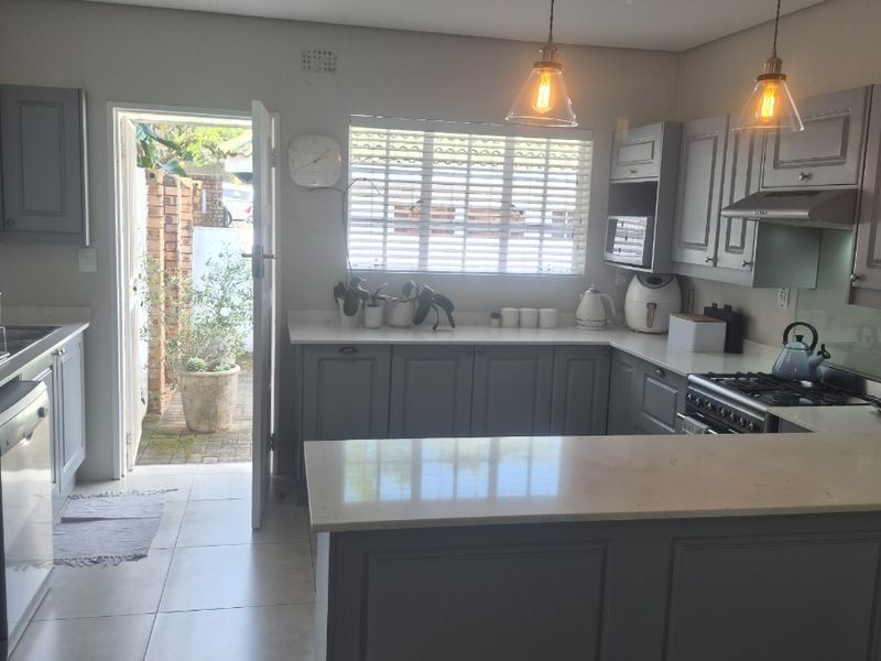 Modern U-shaped kitchen featuring grey cabinetry, stone countertops, integrated appliances, and pendant lighting, with direct access to an outdoor area.