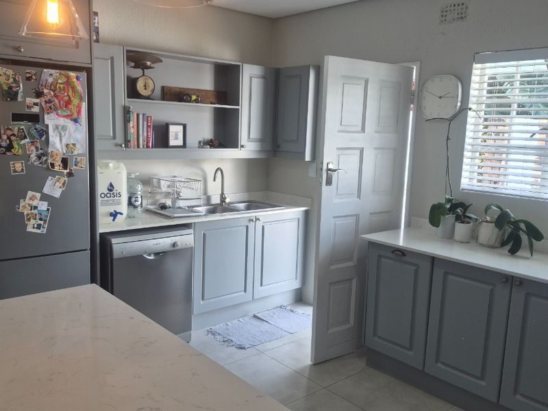 A well-maintained kitchen featuring grey cabinetry, quartz countertops, stainless steel sink, integrated dishwasher, and modern pendant lighting.
