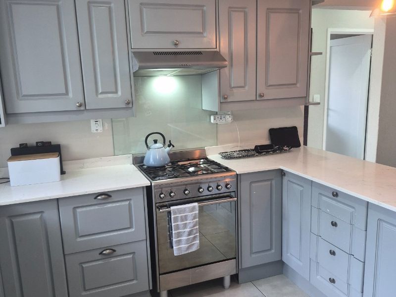 Modern kitchen featuring grey shaker-style cabinetry, stone countertops, a gas stove with extractor fan, and neutral tiled flooring.