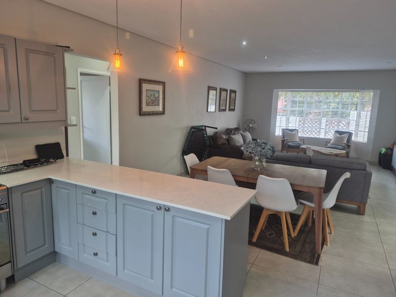 Open-plan living area featuring a modern kitchen with grey cabinetry, stone countertops, and a seamless flow into the dining and lounge space.