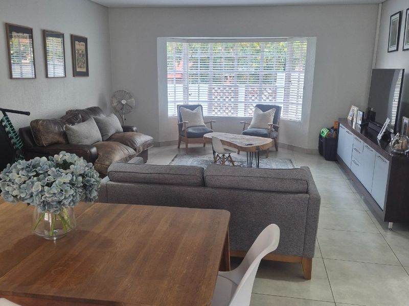 Spacious open-plan living and dining area featuring large bay windows with venetian blinds, recessed downlights, and neutral tiled flooring throughout.