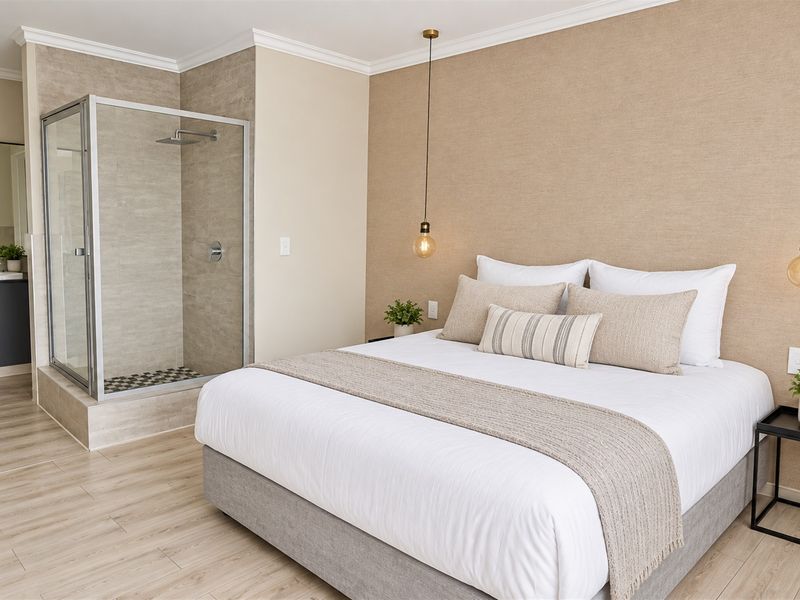 Modern bedroom featuring an open-plan ensuite with a glass-enclosed shower, vanity, and contemporary pendant lighting, finished with neutral tones and laminate flooring.