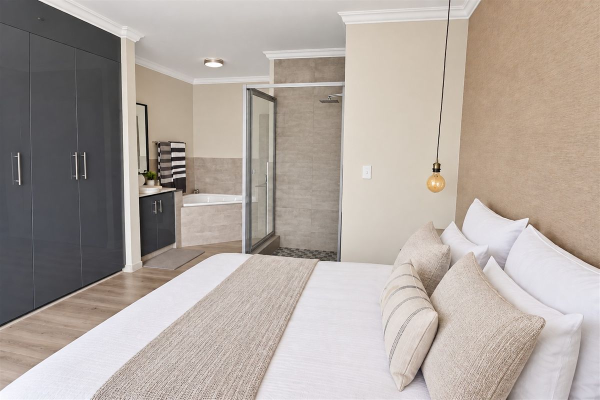 Spacious bedroom featuring modern laminate flooring, extensive built-in cupboards, and a contemporary en-suite bathroom with a glass-enclosed shower and built-in bathtub.