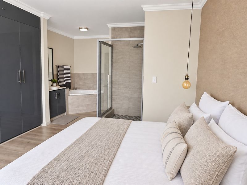 Spacious bedroom featuring modern laminate flooring, extensive built-in cupboards, and a contemporary en-suite bathroom with a glass-enclosed shower and built-in bathtub.