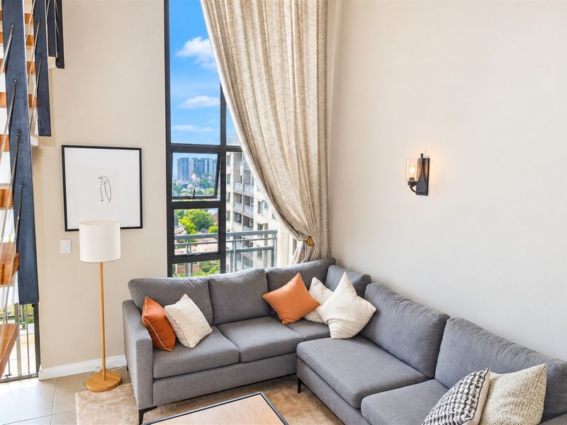 A bright, double-volume living room featuring a full-height window with city views and a modern floating staircase.