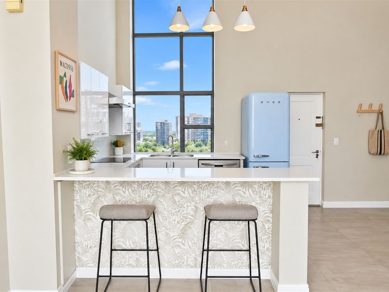 Modern kitchen featuring sleek cabinetry, stone countertops, integrated appliances, and a large window with city views, complemented by a breakfast bar.