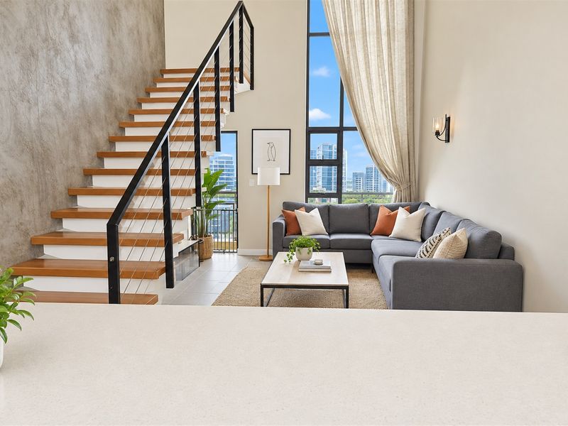 Modern open-plan living area featuring a striking staircase, double-height windows with city views, and high-quality contemporary finishes.
