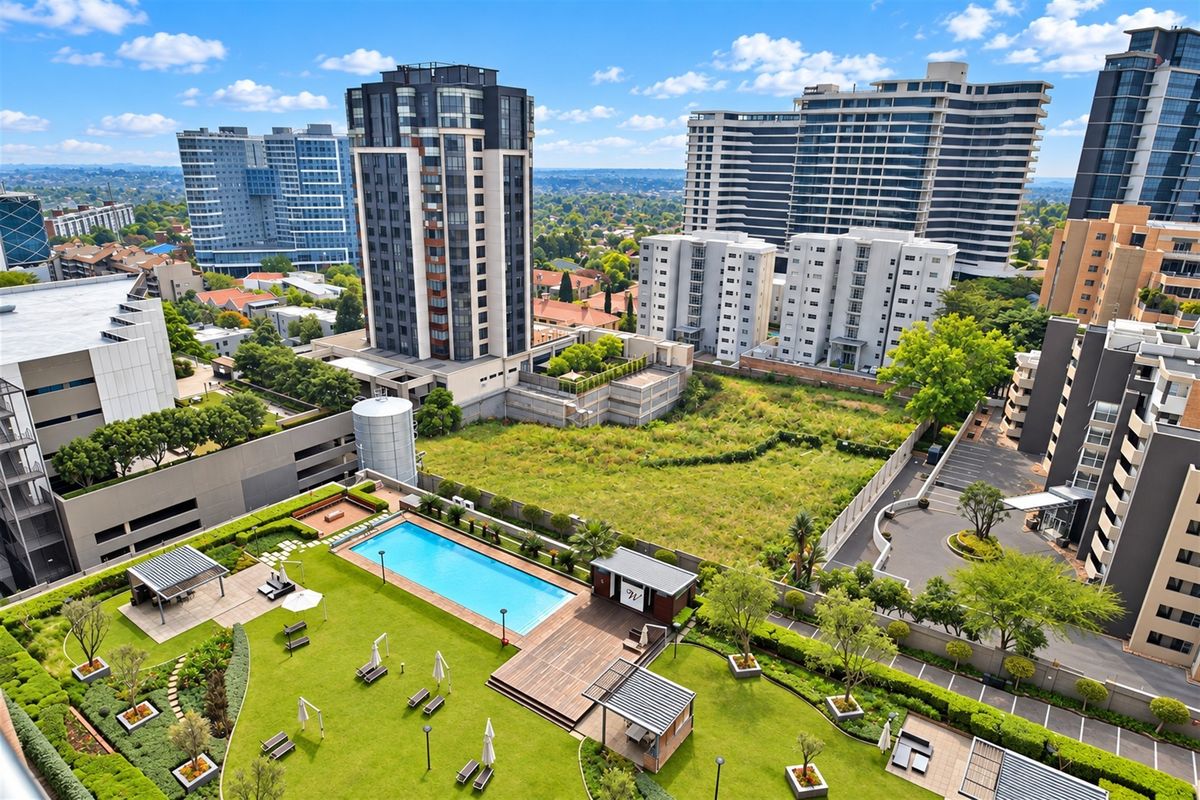 Aerial view of a well-maintained apartment complex rooftop featuring a swimming pool, landscaped gardens, wooden decking, and shaded pergola areas.