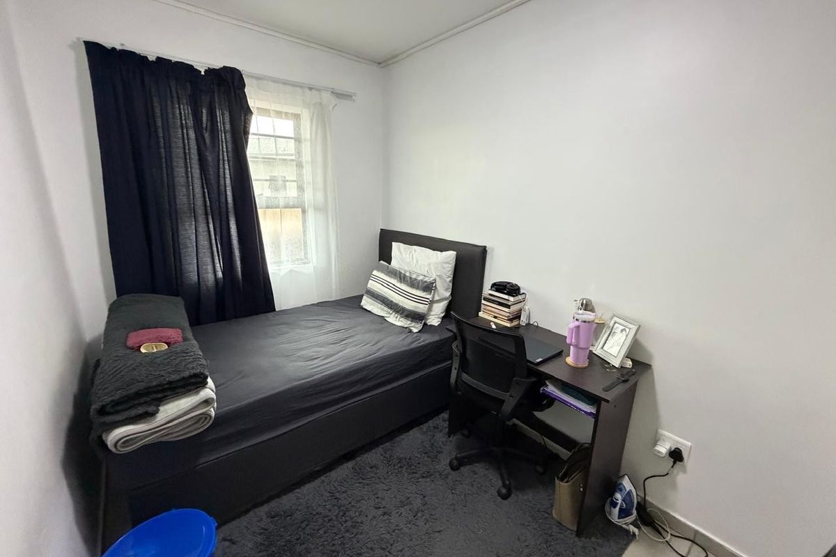 A compact bedroom featuring tiled flooring and a window, providing a functional space for a single bed and study area.