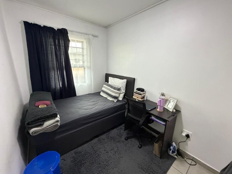 A compact bedroom featuring tiled flooring and a window, providing a functional space for a single bed and study area.