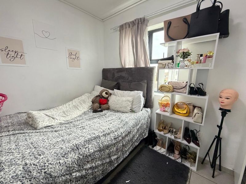 A compact bedroom featuring a window with neutral curtains and tiled flooring, offering a functional space for a single bed.