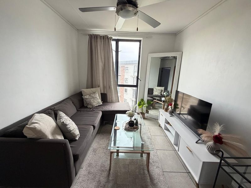 A compact living room featuring tiled flooring, a ceiling fan, and a large window providing natural light.