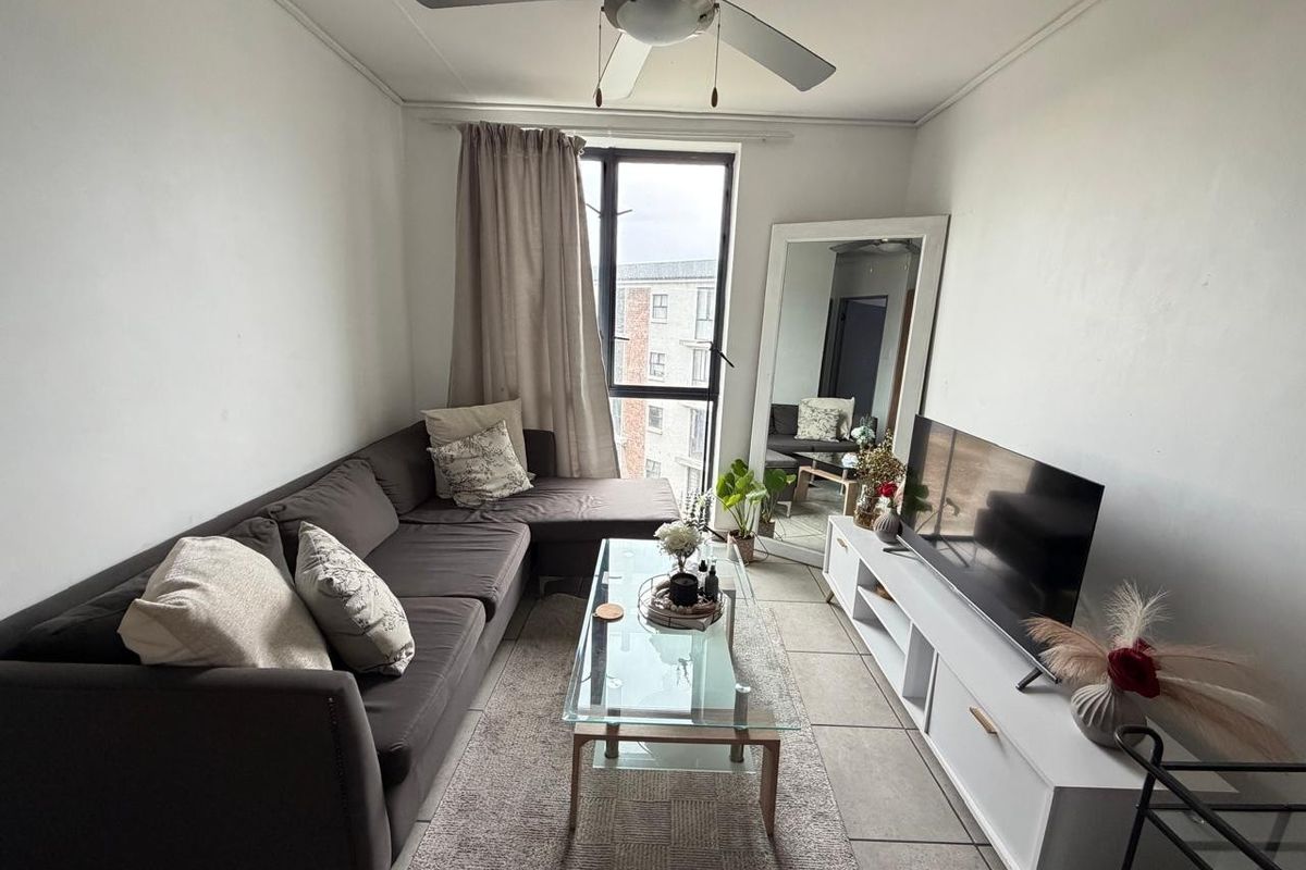 A compact living room featuring tiled flooring, a ceiling fan, and a large window providing natural light.