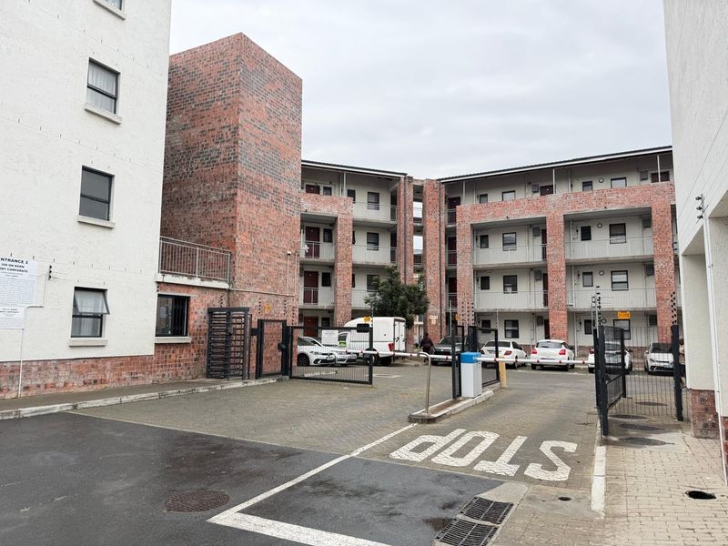 Exterior view of the apartment complex entrance featuring brick facade, secure gated access with boom gate, and paved driveway.