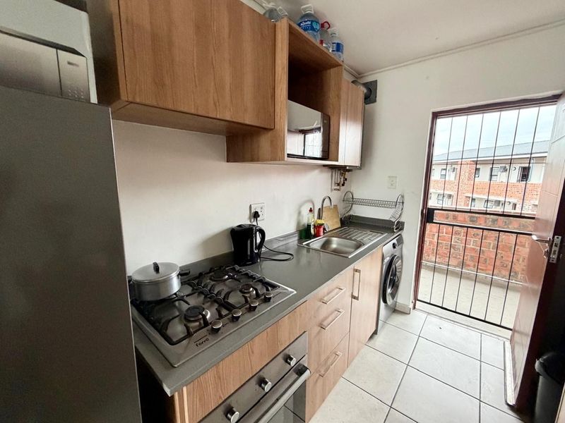 Compact kitchen featuring wood-look cabinetry, gas hob, built-in oven, and tiled flooring, with direct access to an exterior balcony area.