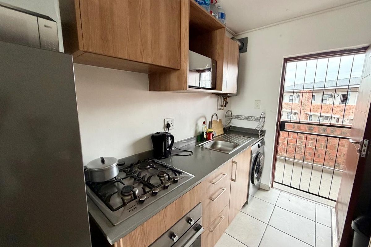 Compact kitchen featuring wood-look cabinetry, gas hob, built-in oven, and tiled flooring, with direct access to an exterior balcony area.