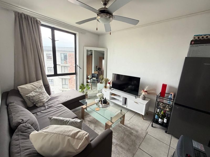 A comfortable living room featuring tiled flooring, a ceiling fan, and a large window providing natural light and an urban view.