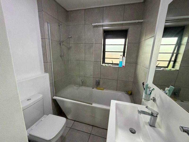 A functional bathroom featuring a bathtub with a glass shower screen, a modern vanity basin, and neutral wall and floor tiling.