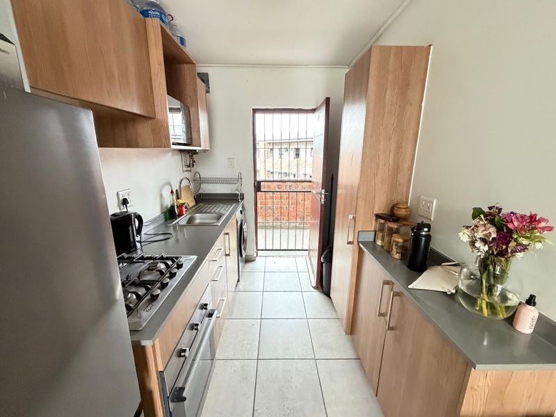 Compact galley-style kitchen featuring wood-finish cabinetry, gas hob, built-in oven, and direct access to an exterior area through a security gate.