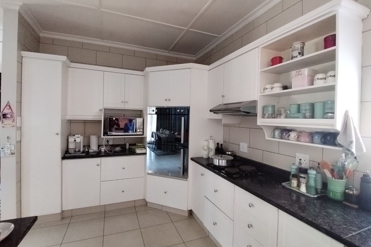 A well-maintained kitchen featuring white cabinetry, dark granite countertops, built-in oven, extractor fan, and tiled finishes throughout.