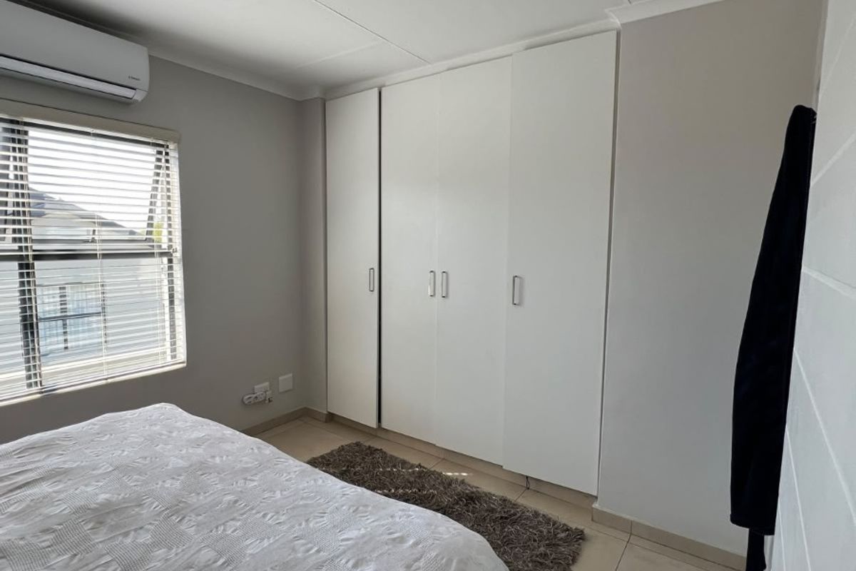 A clean, well-maintained bedroom featuring neutral tiled flooring, built-in white cupboards, and an integrated air conditioning unit.