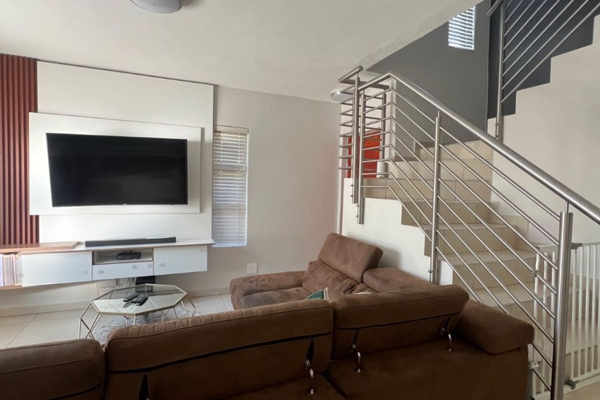 A modern living room featuring a built-in media console, tiled flooring, and a staircase with a contemporary stainless steel balustrade.