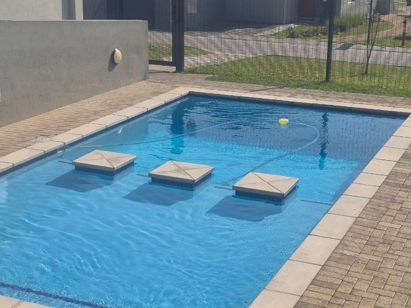 A rectangular swimming pool featuring built-in stone steps, surrounded by paved decking and enclosed by secure mesh fencing in a residential setting.