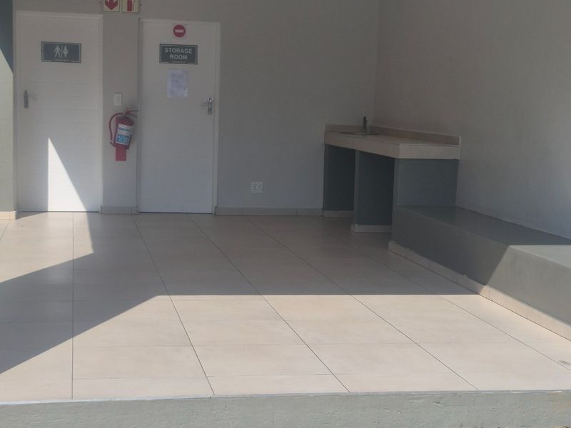 A clean, covered utility area featuring tiled flooring, a built-in concrete counter, and access to a storage room and restroom facilities.