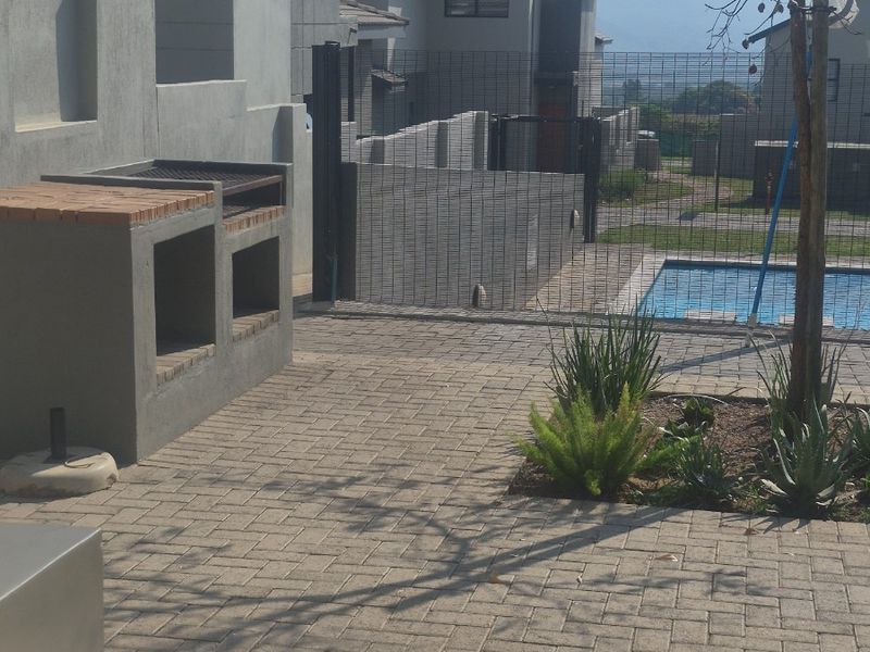 Outdoor patio area featuring a built-in braai, paved flooring, and direct access to a swimming pool within a secure residential estate.