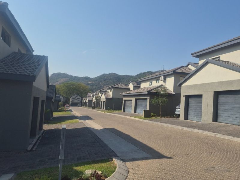 A view of a residential street within a housing estate, featuring paved driveways, modern garage doors, and tiled roof structures.
