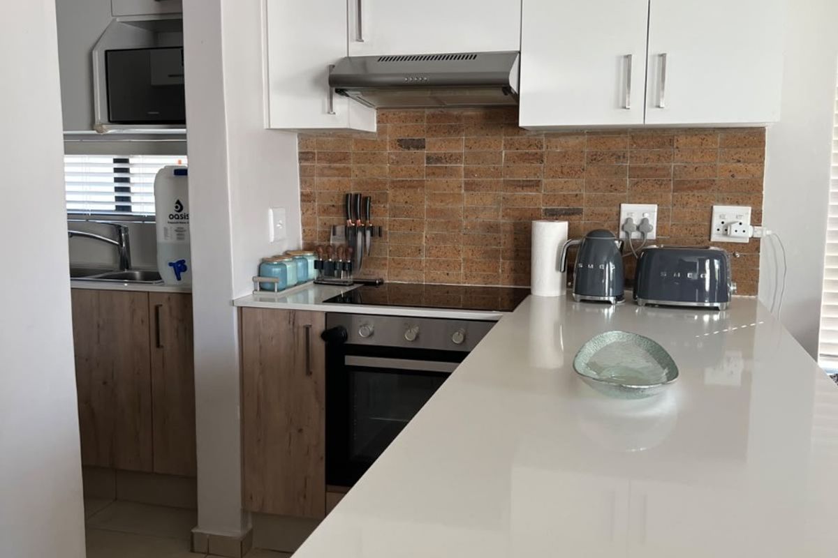 Modern kitchen featuring light wood-finish cabinetry, white stone countertops, a tiled backsplash, and integrated appliances including an oven and hob.