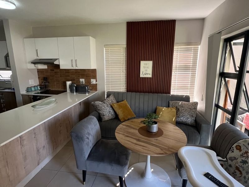 Modern open-plan kitchen and living area featuring sleek cabinetry, stone countertops, tiled flooring, and a decorative slatted wall accent.