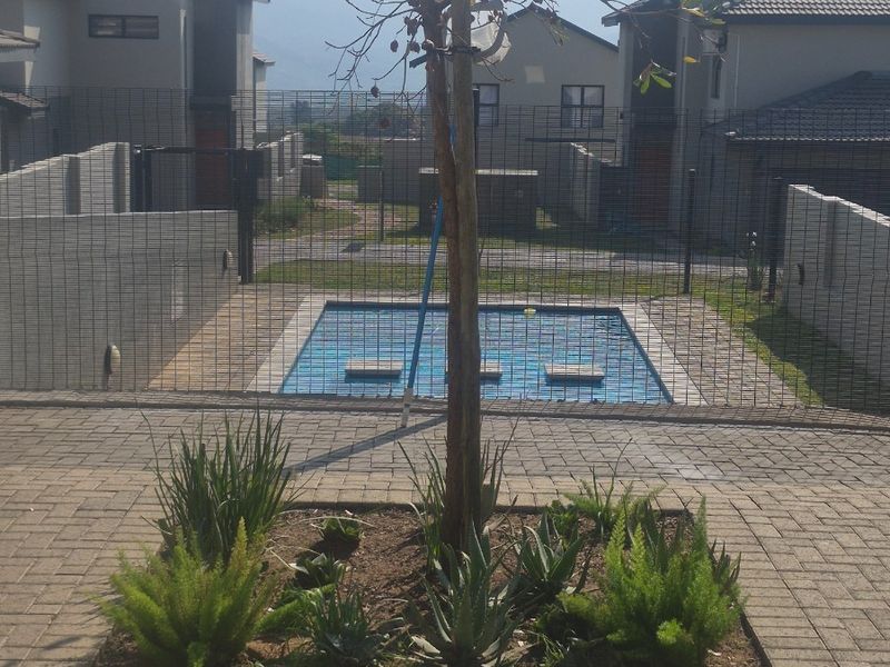 A private swimming pool area featuring paved surrounds, mesh security fencing, and a landscaped garden bed with a central tree.