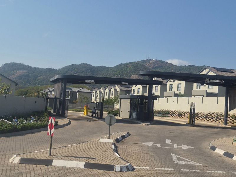 The secure entrance gatehouse of Matumi Valley estate, featuring paved access roads, boom gates, and perimeter security fencing against a mountain backdrop.