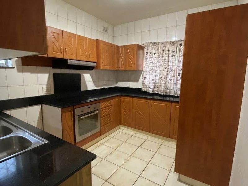A functional kitchen featuring wooden cabinetry, black granite countertops, built-in oven, extractor fan, and tiled flooring with a neutral backsplash.