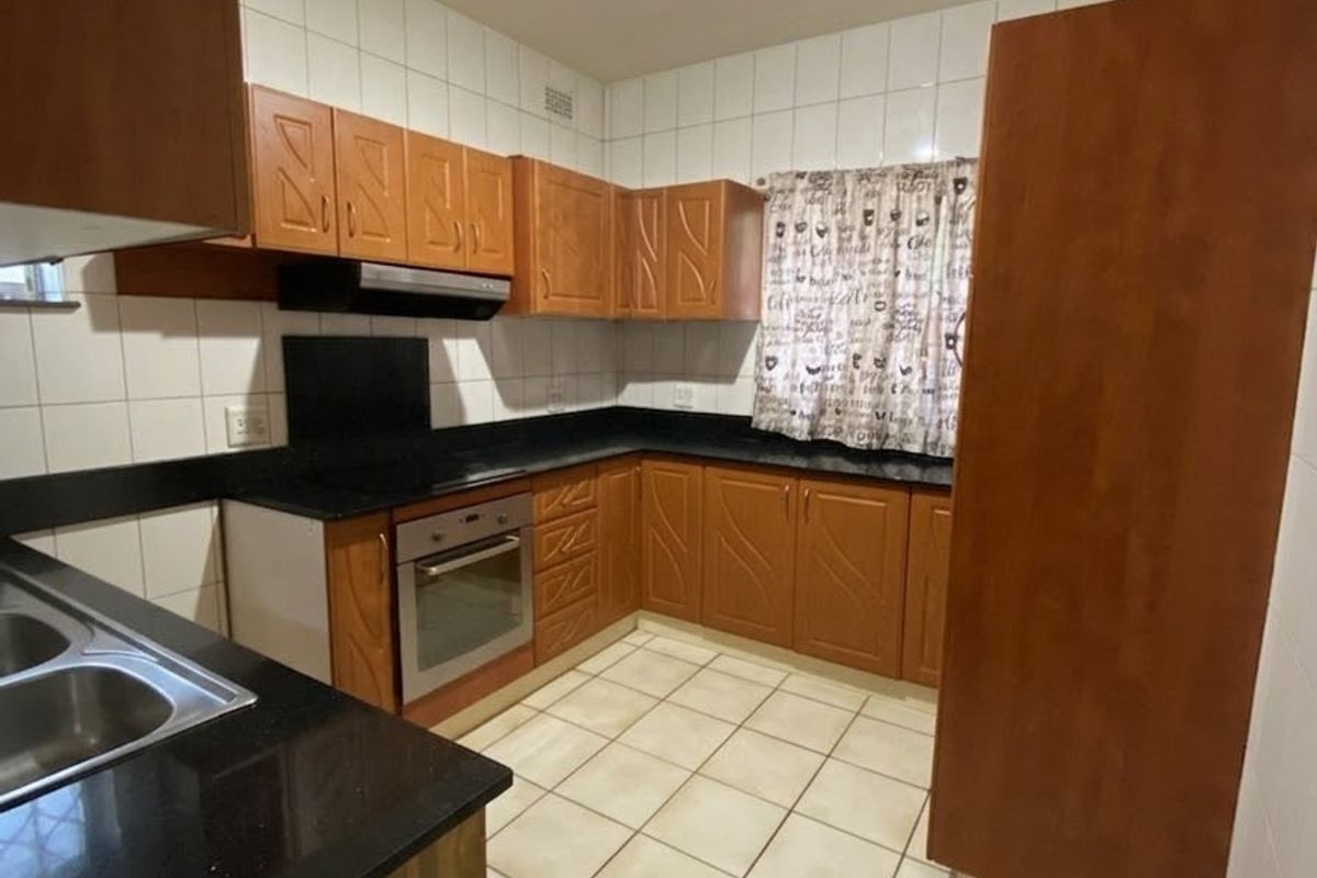 A functional kitchen featuring wooden cabinetry, black granite countertops, built-in oven, extractor fan, and tiled flooring with a neutral backsplash.