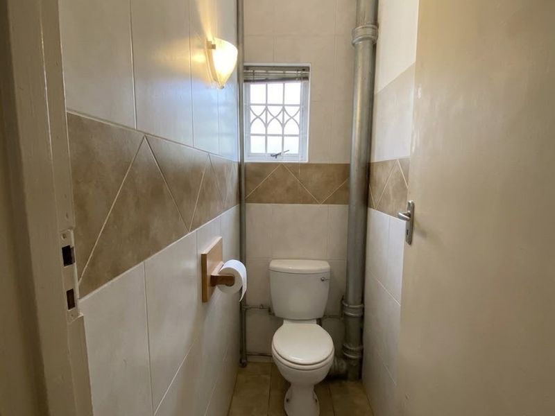 A compact guest bathroom featuring ceramic wall and floor tiles, a standard toilet, and an exposed vertical plumbing pipe.