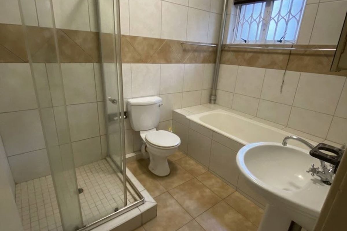 A functional bathroom featuring a glass shower enclosure, a built-in bathtub, a pedestal basin, and a toilet with neutral wall and floor tiling.