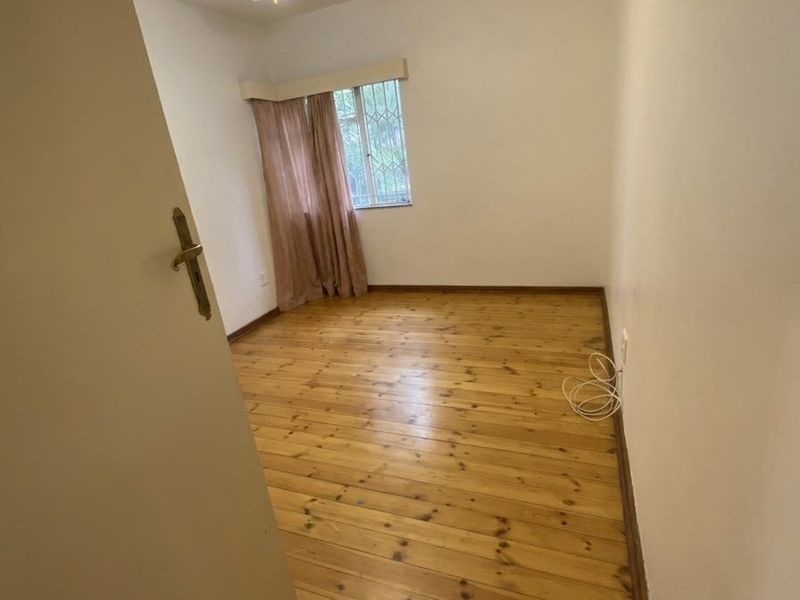 A bright, empty bedroom featuring polished timber flooring, a ceiling fan, and security bars on the window.