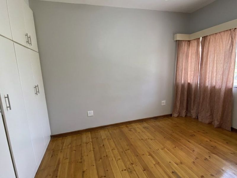 A bright, empty bedroom featuring polished timber flooring, built-in storage cupboards, and a ceiling fan.
