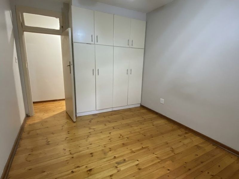 A bright, empty bedroom featuring polished timber flooring, built-in storage cupboards, and a ceiling fan.