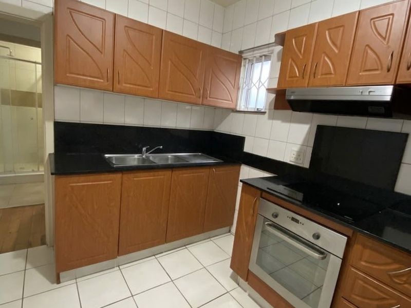 A functional kitchen featuring wooden cabinetry, granite countertops, built-in oven, hob, and extractor fan with tiled finishes throughout.