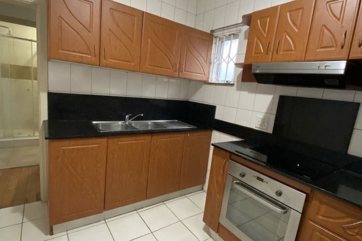 A functional kitchen featuring wooden cabinetry, granite countertops, built-in oven, hob, and extractor fan with tiled finishes throughout.