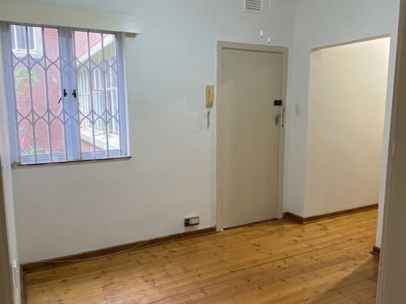 An empty bedroom featuring original hardwood flooring, a ceiling fan, and a window fitted with a security gate.
